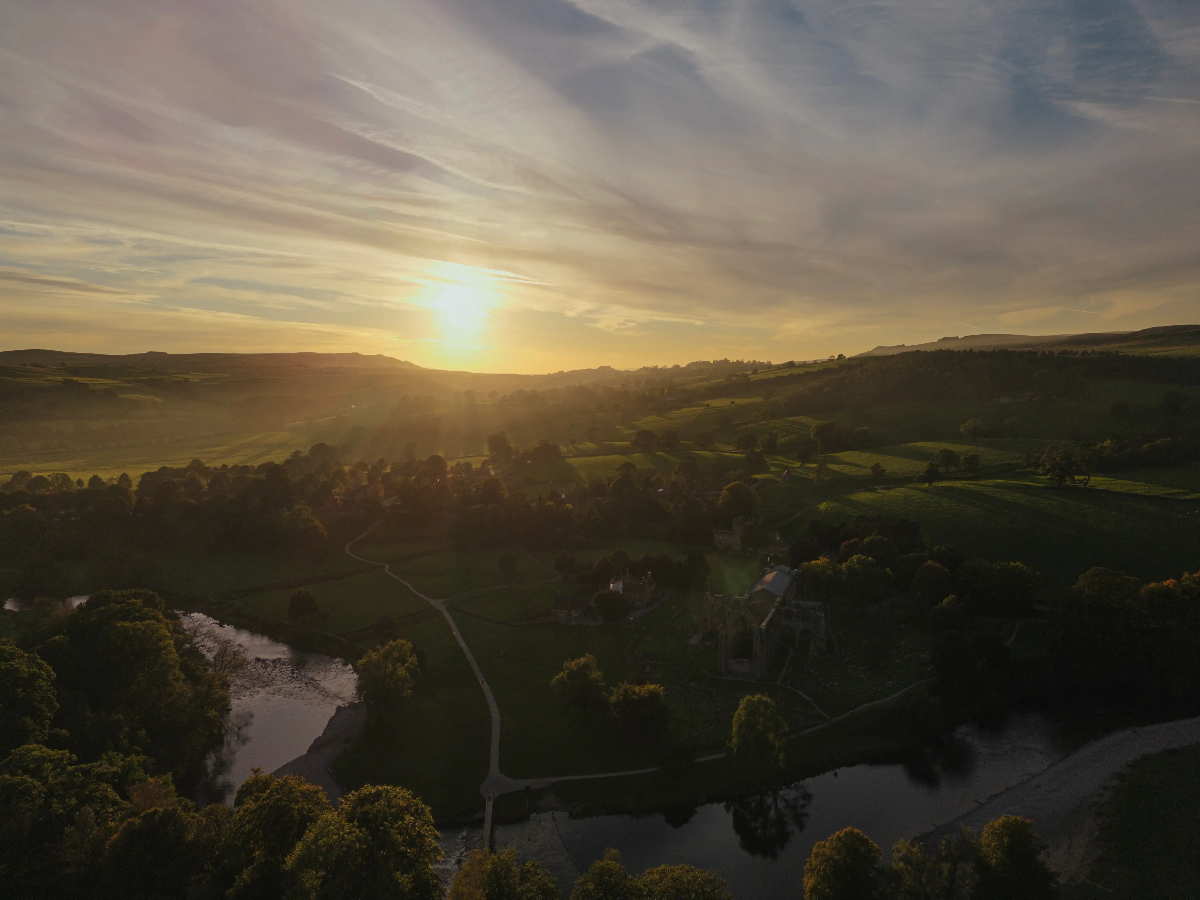 Aerial view of historic 12th-century Bolton Abbey priory illuminated by warm sunset light