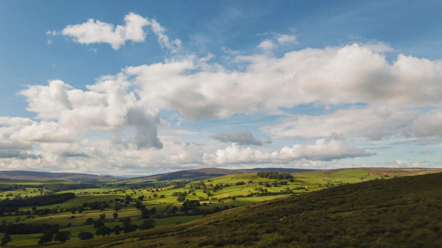Vast aerial view of patchwork green fields, rolling hills, and dry stone walls in Yorkshire